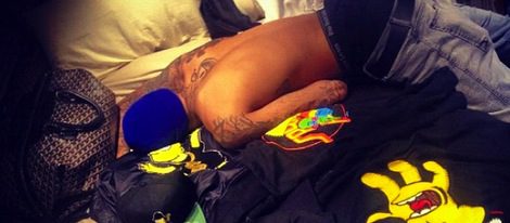 Chris Brown tirado en la cama entre accesorios de Bart Simpson