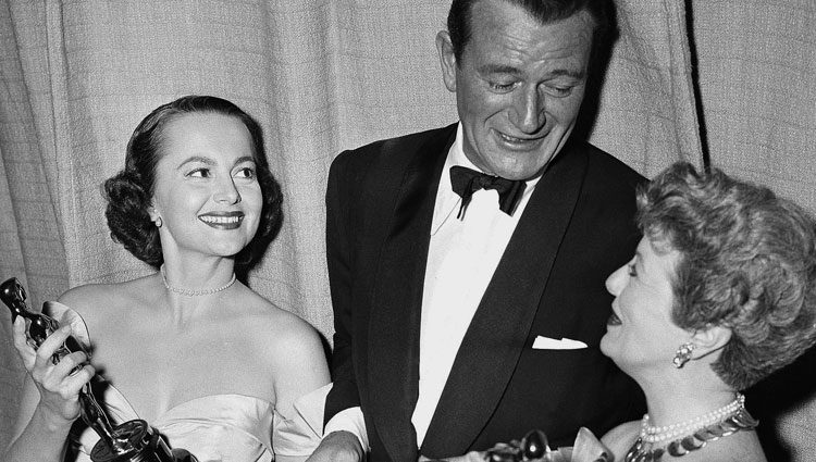 Olivia de Havilland recogiendo su Oscar junto a John Wayne