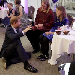 El Príncipe Harry sentado en el suelo hablando con una mujer y una niña en un acto oficial