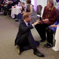El Príncipe Harry sentado en el suelo hablando con una mujer y una niña en un acto oficial