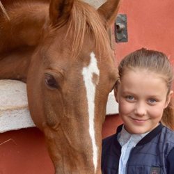 Isabel de Dinamarca sonriente junto a un caballo en su onceavo cumpleaños