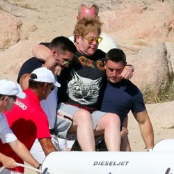 Elton John siendo ayudado para subirse a una pequeña embarcación en Cerdeña