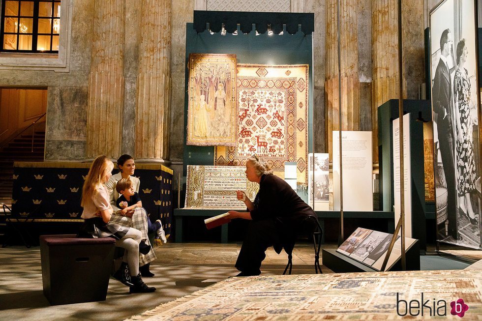 Victoria de Suecia y sus hijos Estela y Oscar de Suecia escuchan explicaciones en una exposición de alfombras