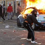 Un joven protagonista de los disturbios de Londres junto a un coche en llamas