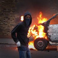 Un encapuchado junto a una furgoneta en llamas en los disturbios de Londres