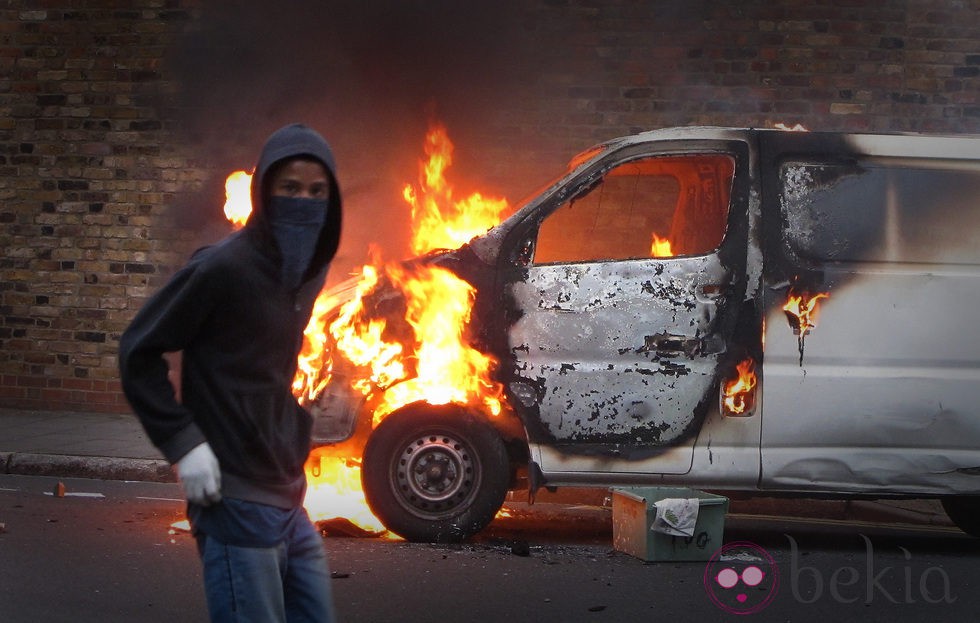 Un encapuchado junto a una furgoneta en llamas en los disturbios de Londres