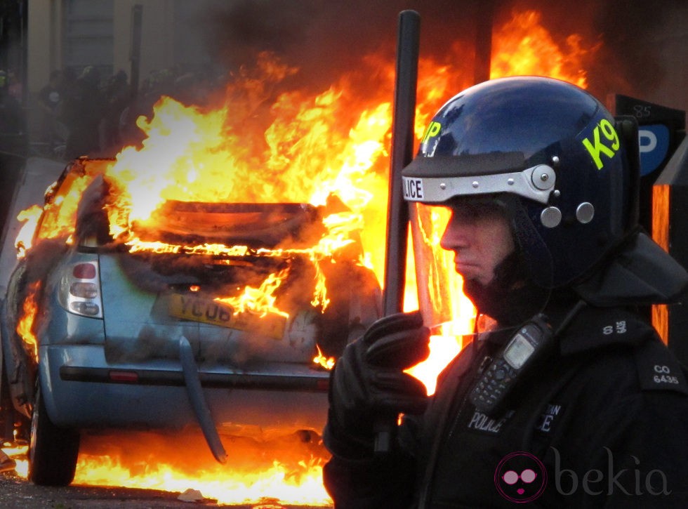 Un policía junto a un coche en llamas en los disturbios de Londres
