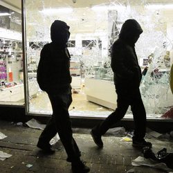 Dos jóvenes caminan junto a una tienda saqueada en los disturbios de Londres