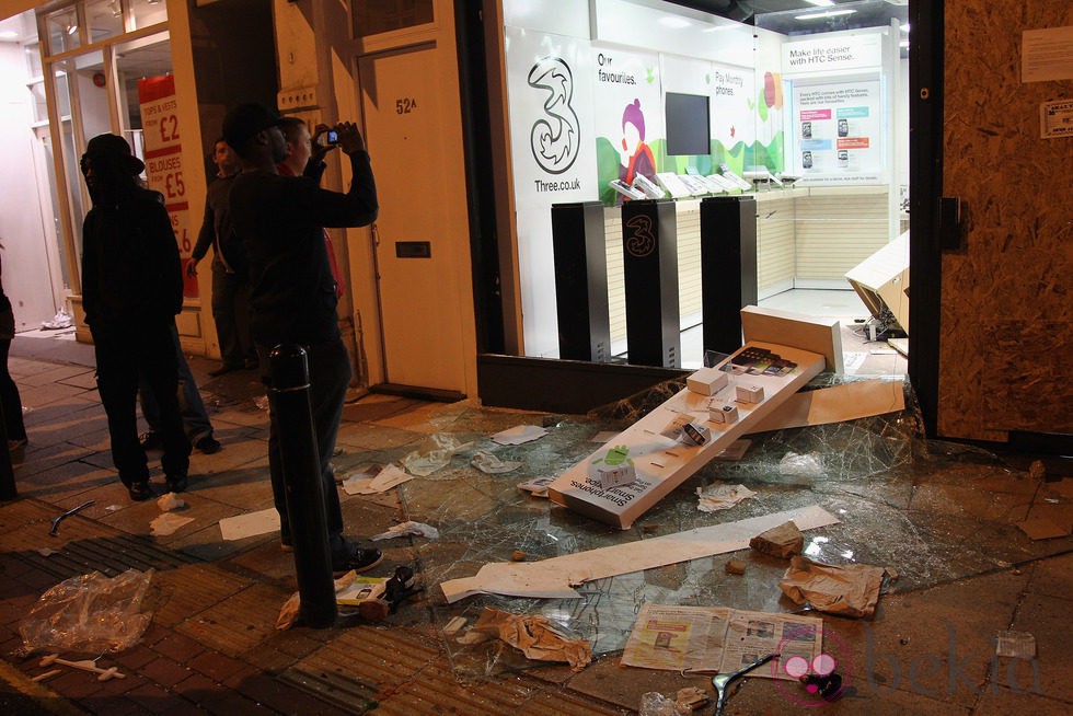 Varias personas fotografían una tienda saqueada en los disturbios de Londres