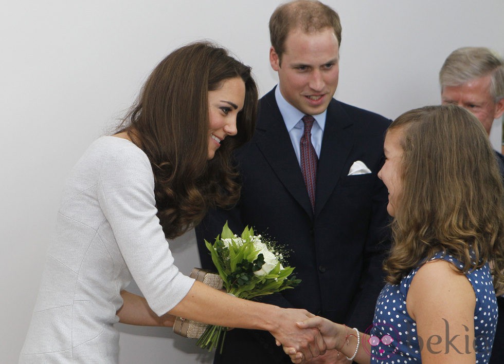 Una niña entrega unas flores a Catalina de Cambridge junto al Príncipe Guillermo en un hospital