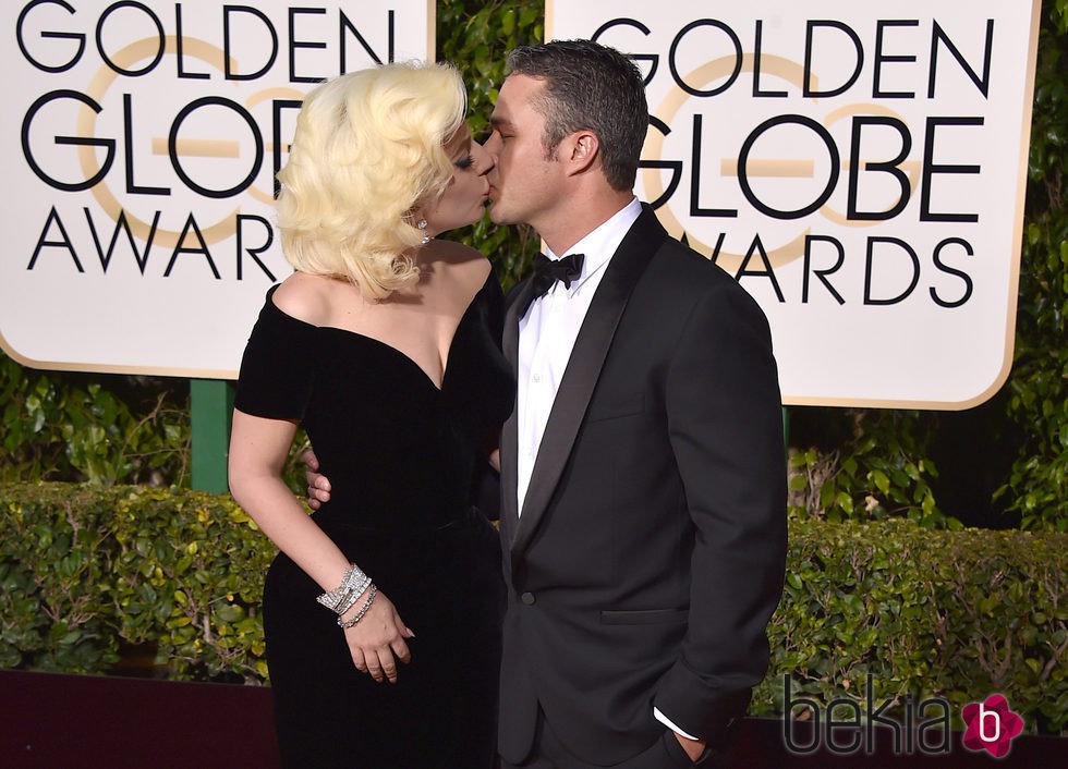 Lady Gaga y Taylor Kinney besándose en la alfombra roja de los Globos de Oro 2016