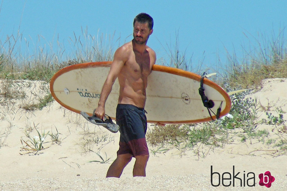 Hugo Silva con el torso desnudo y una tabla de surf